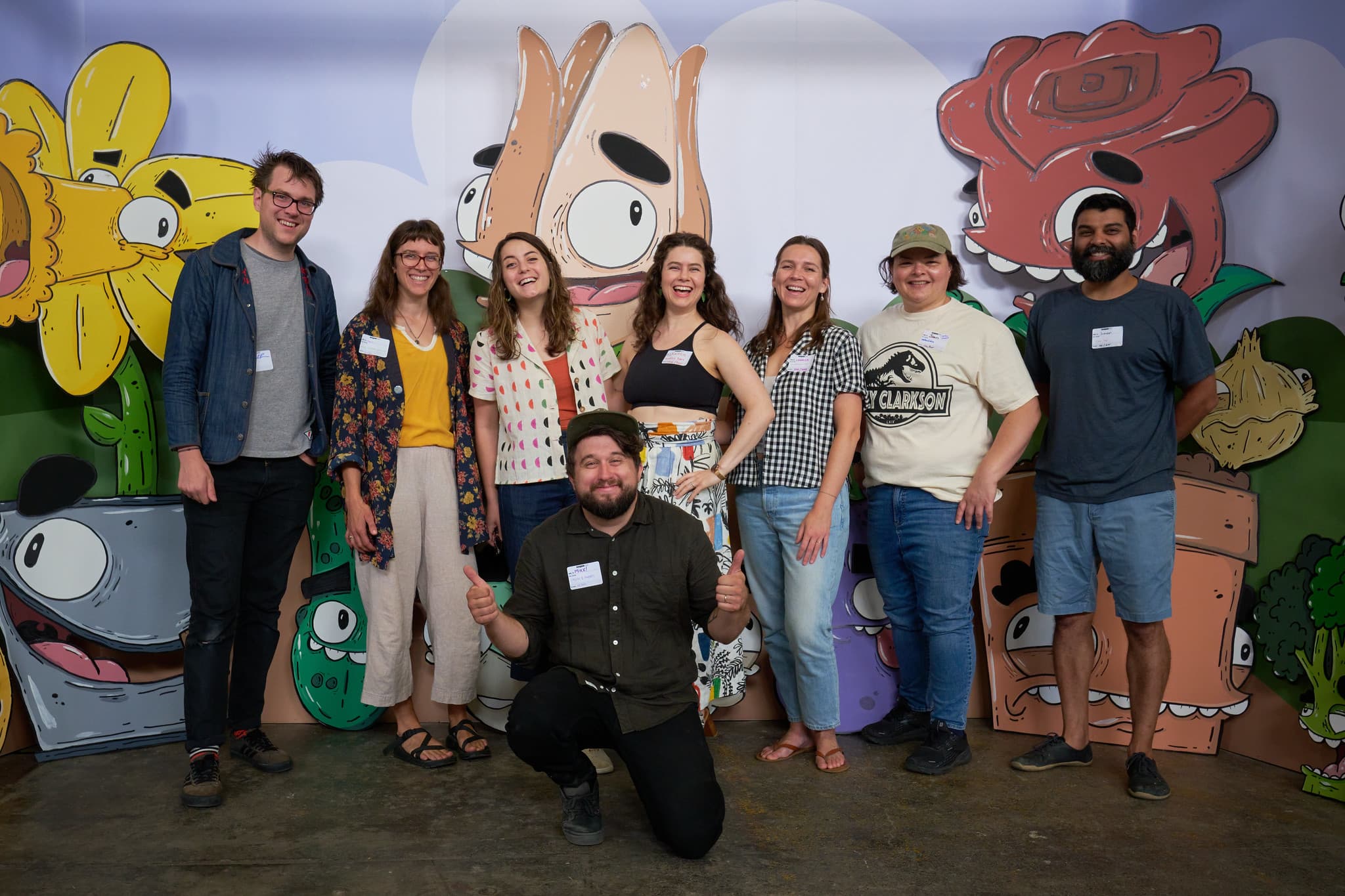 Kaitlin and six other members of the CreativeMornings Portland team posing with Mike Bennett in front of his large illustrations of anthropomorphic flowers