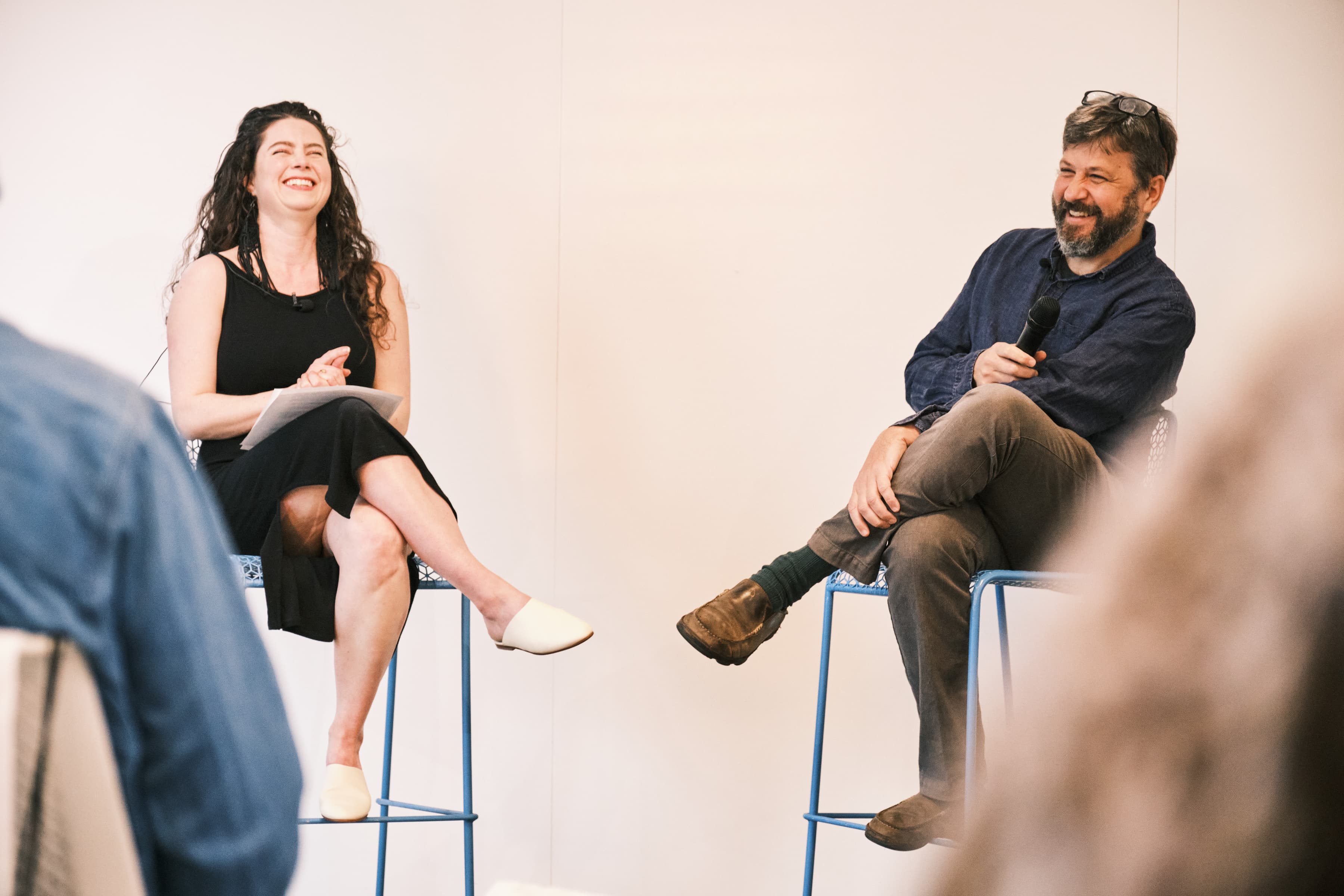 Kaitlin Carpenter and David Naimon seated on barstools and holding microphones. Both are laughing.